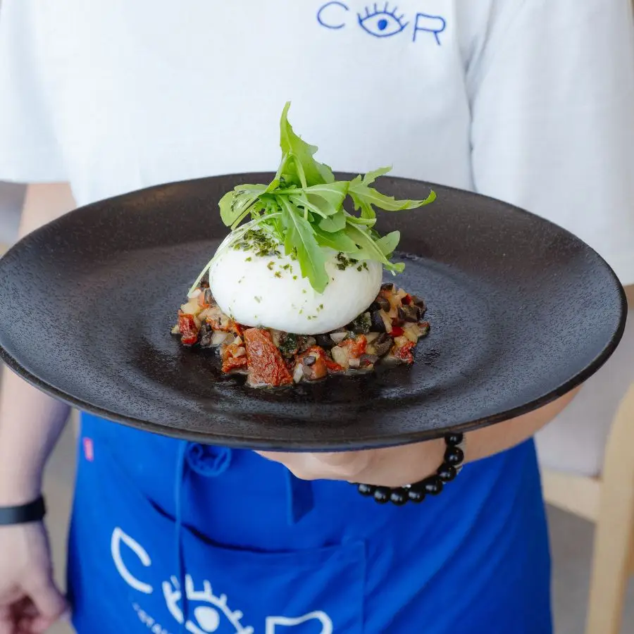 Camarero de COR presentando un plato con el logo del restaurante, mostrando el cuidado en emplatado y servicio